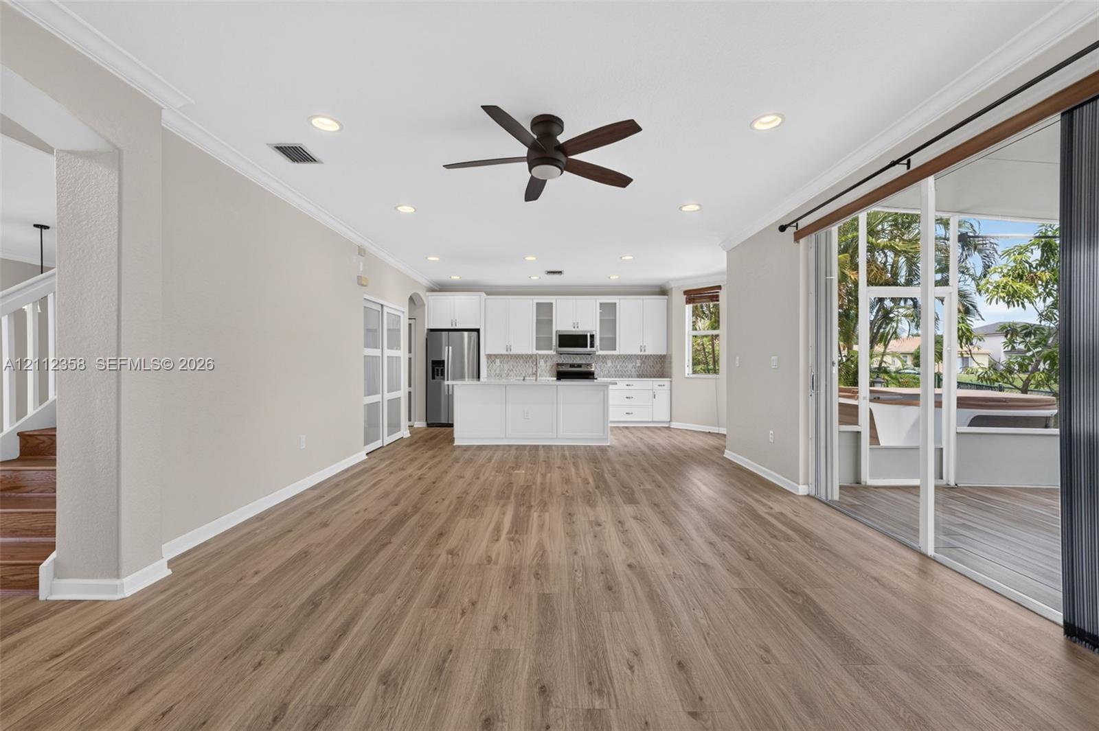 Open-concept interior featuring wood-finish flooring, recessed lighting, a center island kitchen with white cabinetry, and multi-panel sliding glass doors