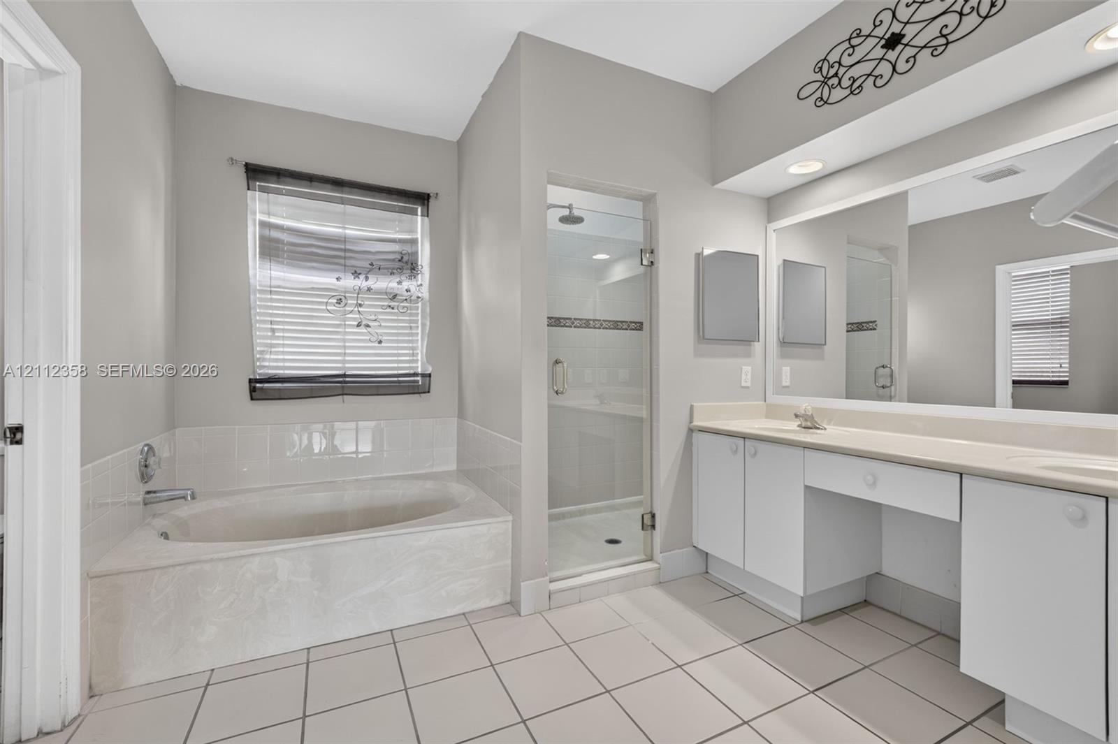 Bathroom featuring a tiled soaking tub with a tiled surround, a separate glass-enclosed shower, dual-sink vanity with white cabinetry, and recessed lighting