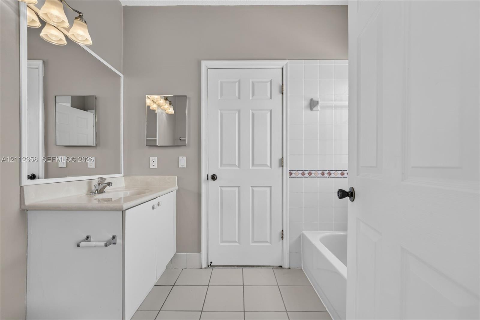 Bathroom featuring a white vanity with a stone countertop, a large wall-mounted mirror, a multi-bulb light fixture, a tiled shower-tub combination, and neutral ceramic tile flooring