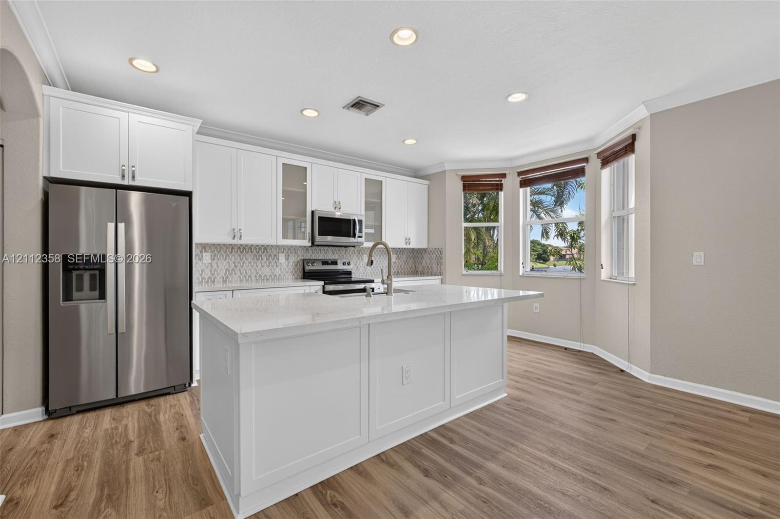Kitchen featuring white cabinetry with glass-front display panels, stone-finish countertops, stainless steel appliances, a center island with a built-in sink, and wood-finish flooring