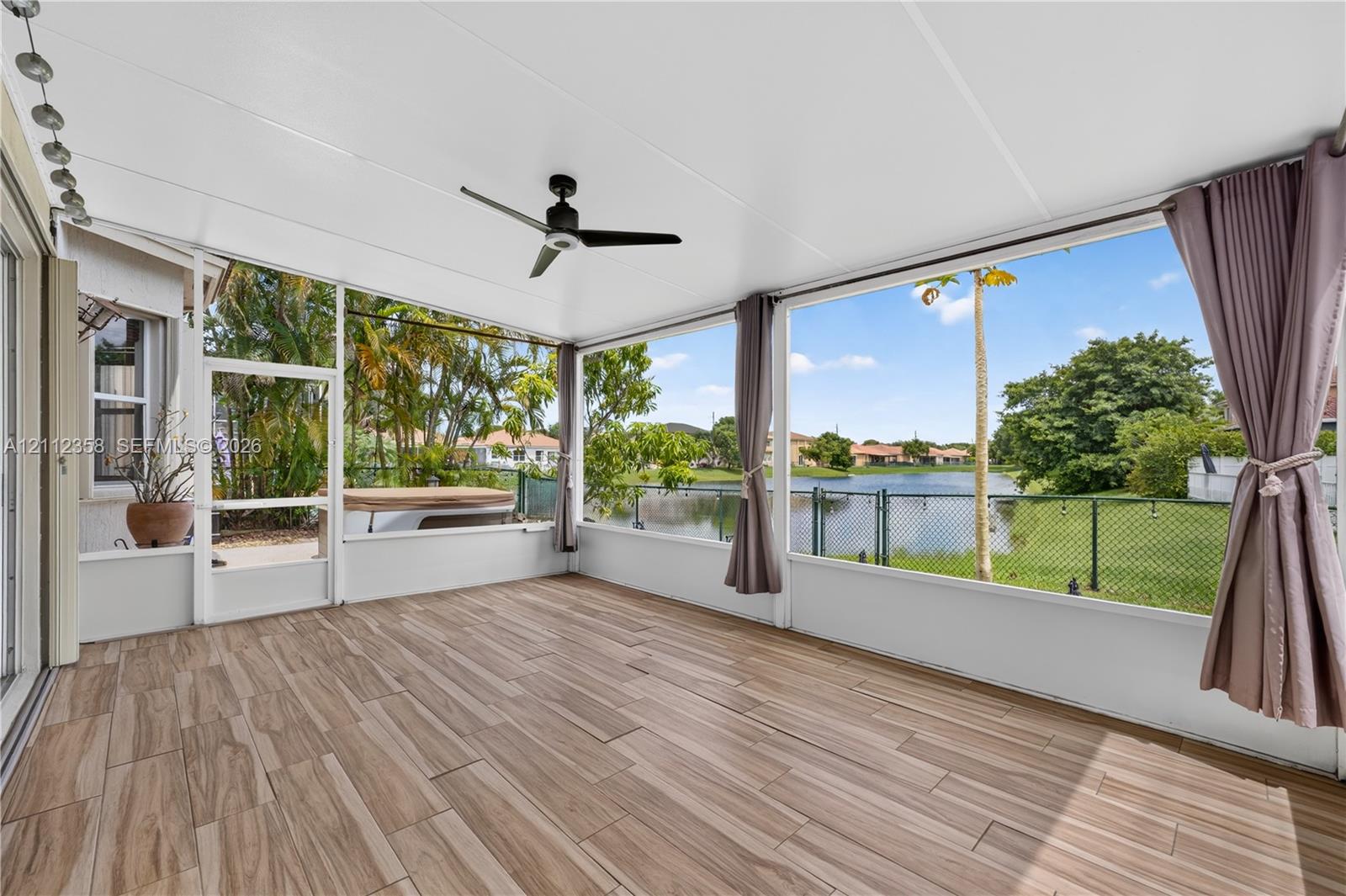 Screened-in lanai featuring wood-finish flooring, a ceiling fan, and large window panels overlooking the water