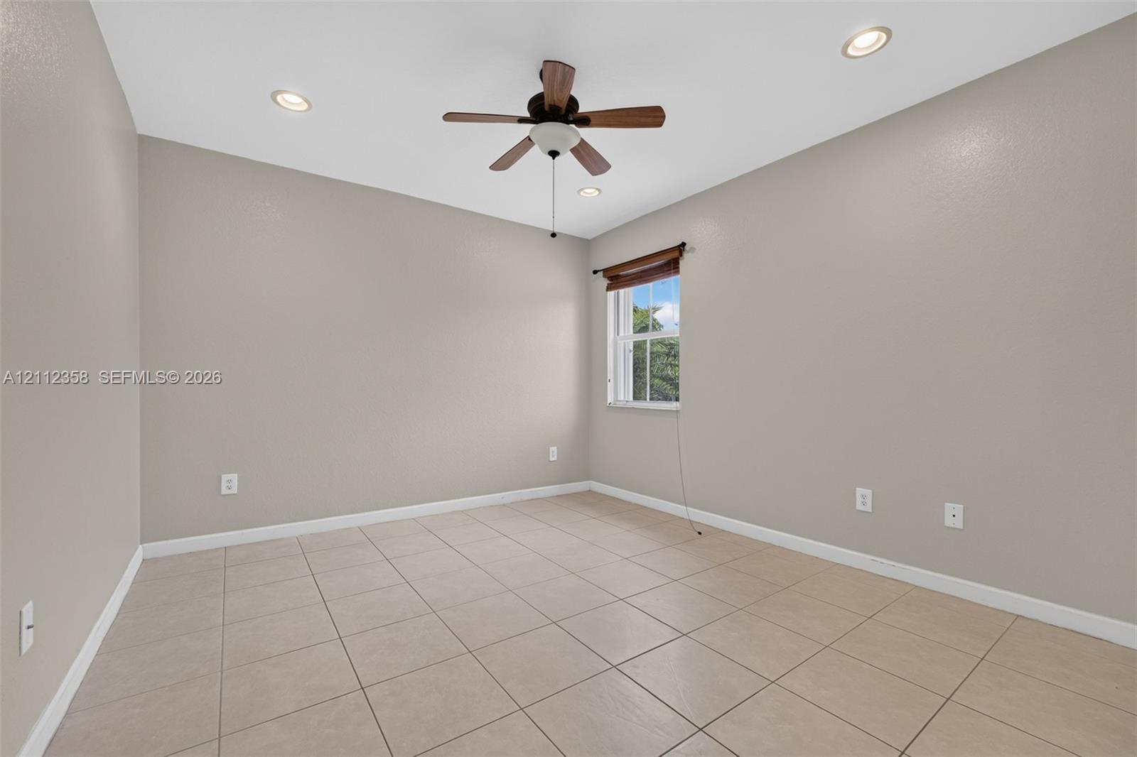 Neutral-toned room featuring large-format tile flooring, recessed lighting, a ceiling fan, and a single window with a wooden valance