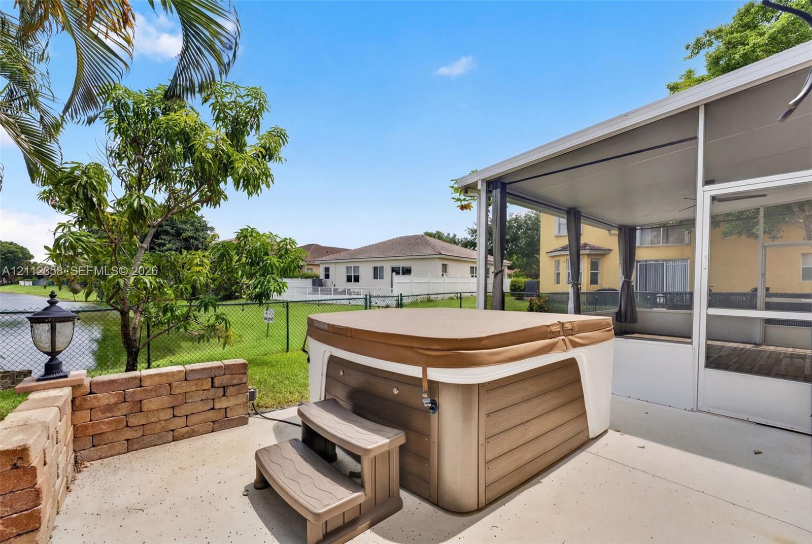 Screened-in patio with a concrete deck, built-in hot tub, brick retaining wall, and fenced backyard bordering water