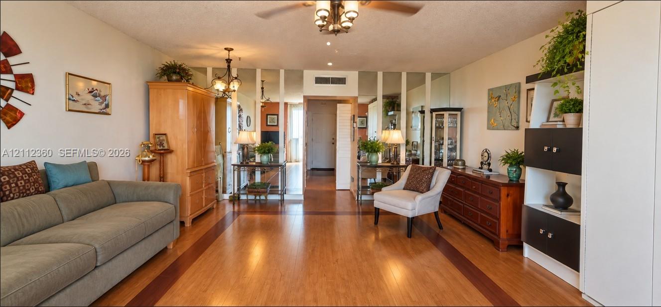 Living area featuring wood-finish flooring with a contrasting perimeter border, mirrored wall panels, and two multi-arm hanging light fixtures