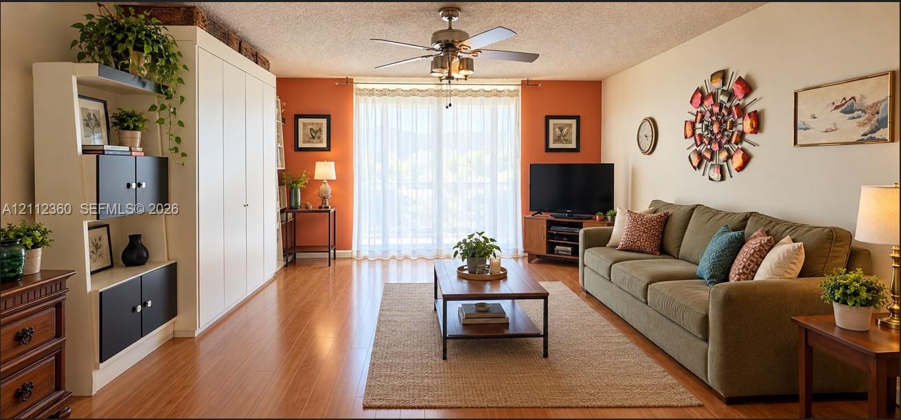 Living area featuring wood-finish flooring, built-in floor-to-ceiling cabinetry, and a ceiling-mounted light fixture with integrated fan