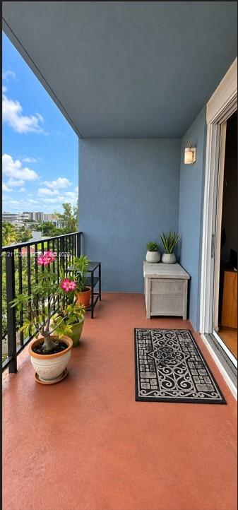Covered balcony featuring a solid surface floor, black metal railing, and wall-mounted exterior lighting
