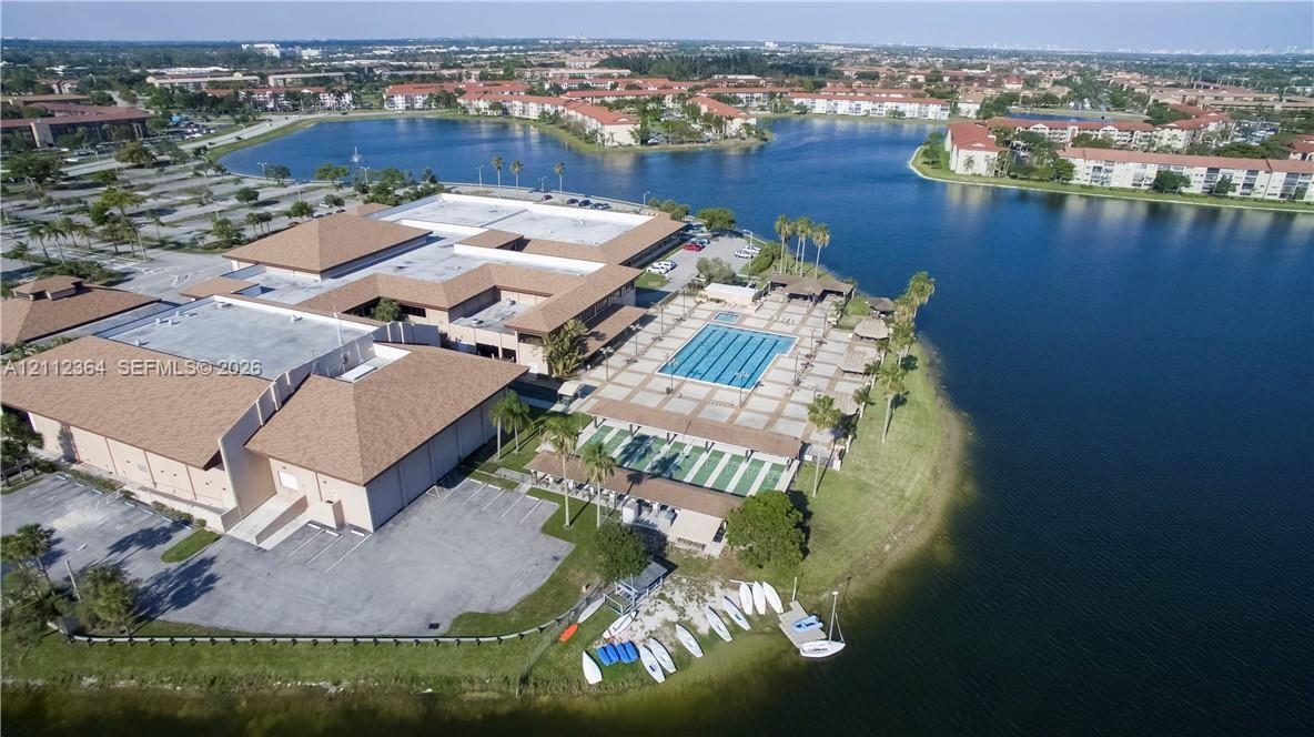Aerial perspective of property grounds featuring a swimming pool, paved patio, multi-use courts, and direct water frontage with a boat launch