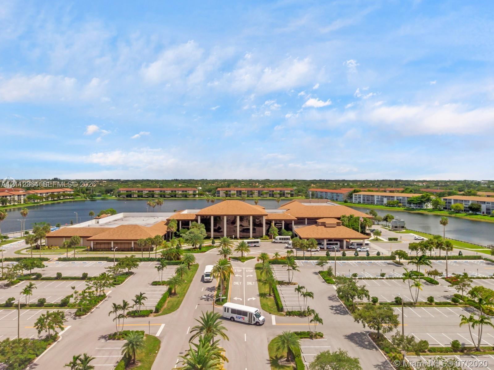 Aerial view of a sprawling complex featuring multiple low-rise buildings, expansive parking facilities, mature palm trees, and waterfront grounds