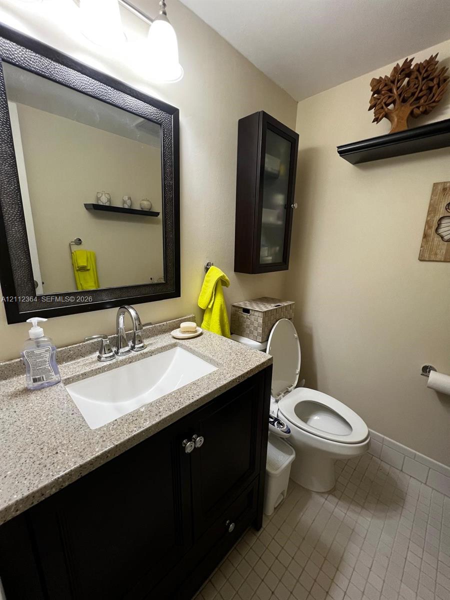 Dark wood vanity with integrated basin and stone-composite countertop, wall-mounted storage cabinetry, framed wall mirror, and neutral tile flooring