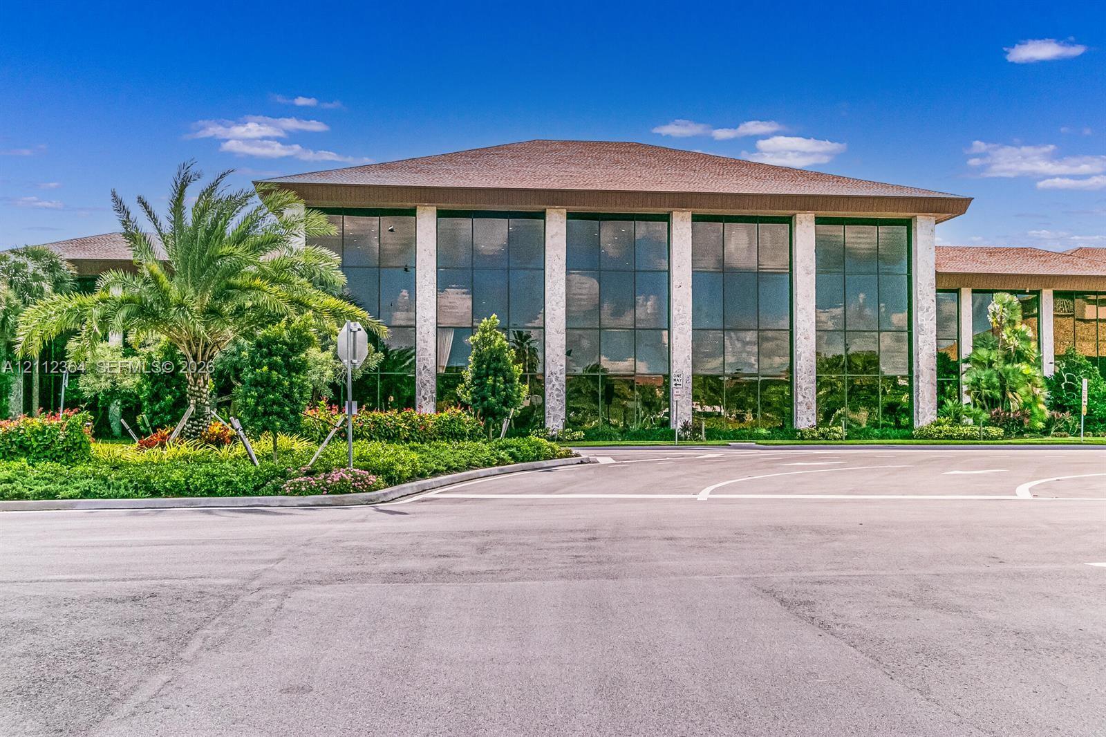 Commercial building exterior featuring extensive glass wall panels, structured stone columns, and a hipped roofline, surrounded by manicured landscaping