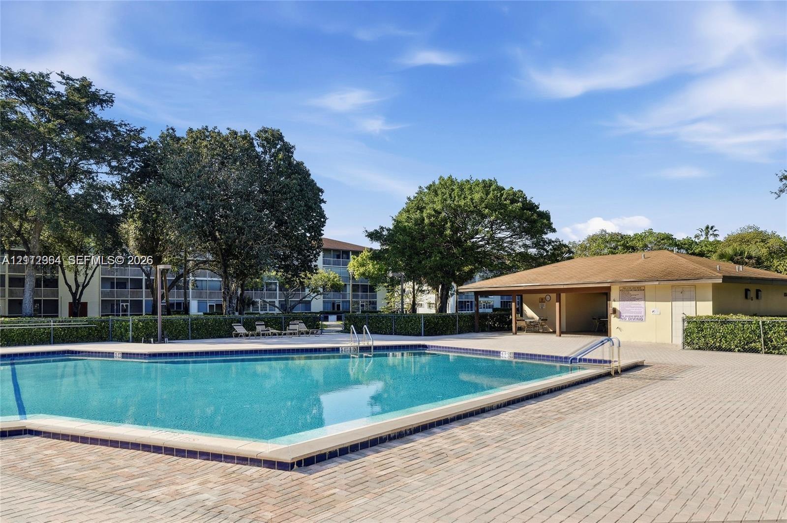 Community swimming pool featuring a tiled perimeter and a concrete paver deck, including a covered pavilion with built-in storage areas and mature trees