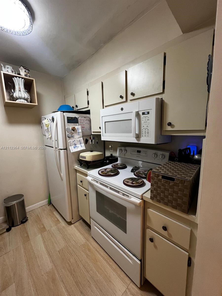 Kitchen featuring flat-panel cabinetry, wood-finish flooring, built-in over-the-range microwave, and white appliances