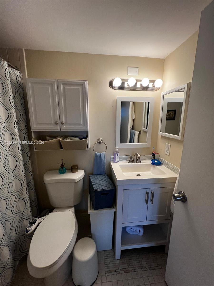 White vanity with rectangular sink, four-light vanity fixture, built-in upper cabinet storage, and framed wall mirror