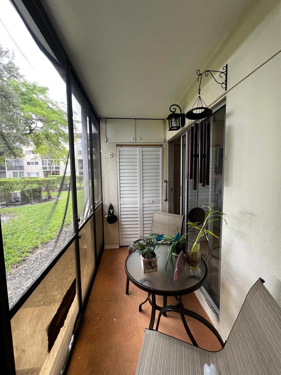 Screened-in balcony featuring louvered-door storage cabinetry, wall-mounted lantern-style exterior lighting, and sliding glass entry