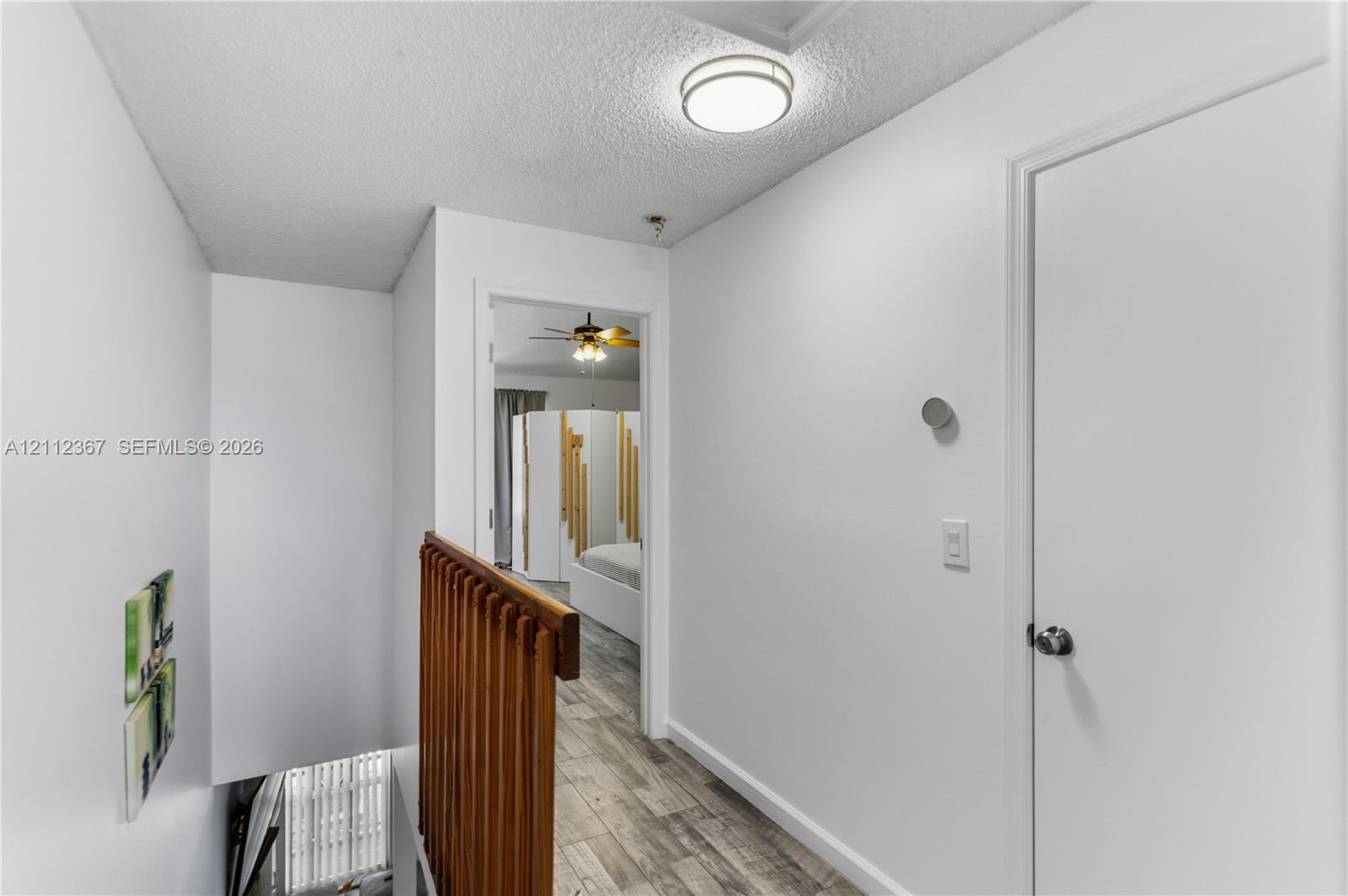 Hallway featuring wood-finish flooring, a wood-slat railing, a flush-mount ceiling light fixture, and a solid-core interior door