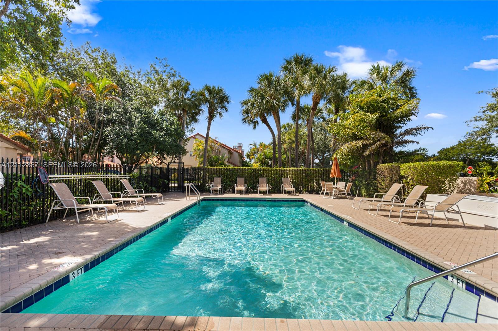 Rectangular swimming pool featuring a brick paver deck, metal safety fencing, and stepped entry