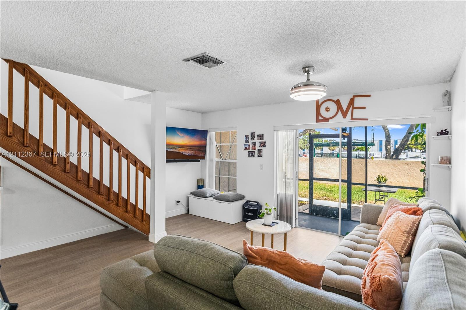 Living area featuring wood-finish flooring, a wooden staircase with integrated railing, a ceiling-mounted light fixture with fan, and a sliding glass door providing external access