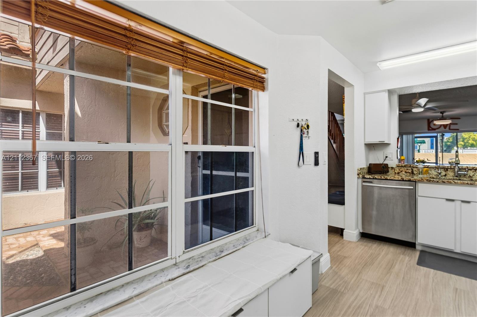 Built-in window seat featuring a solid surface countertop, large multi-pane windows, stainless steel dishwasher, white cabinetry, and wood-finish flooring