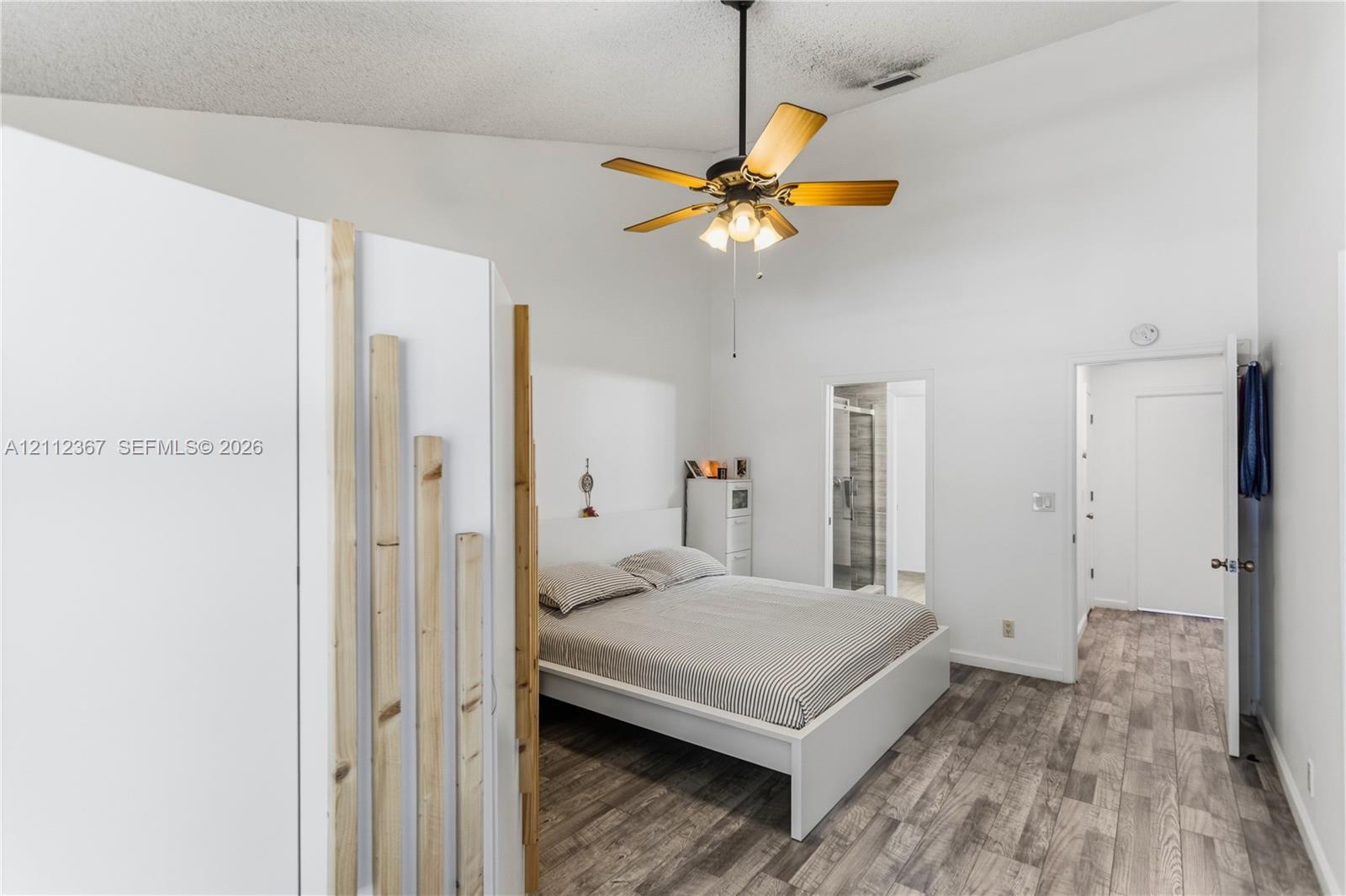 Vaulted ceiling featuring a central multi-blade ceiling fan, wood-finish flooring, and a decorative light wood slat partition