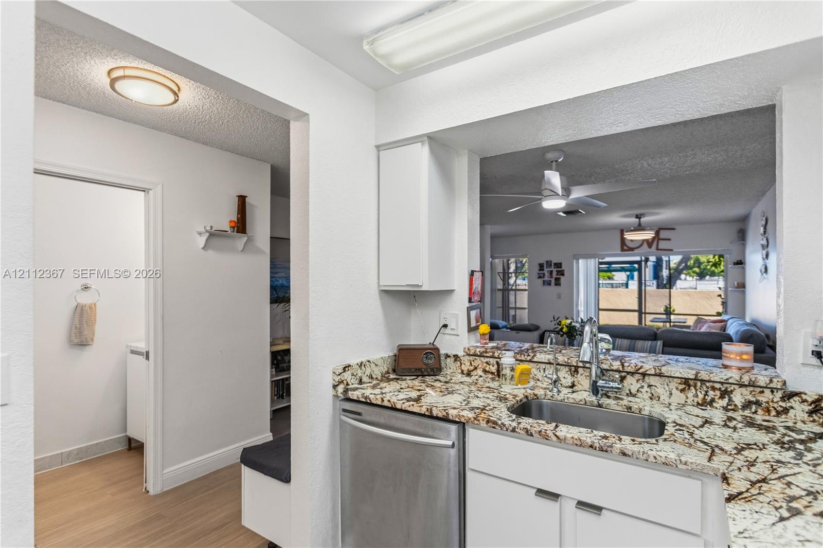 Kitchen featuring stone countertops, stainless steel undermount sink with pull-down faucet, stainless steel dishwasher, and white cabinetry