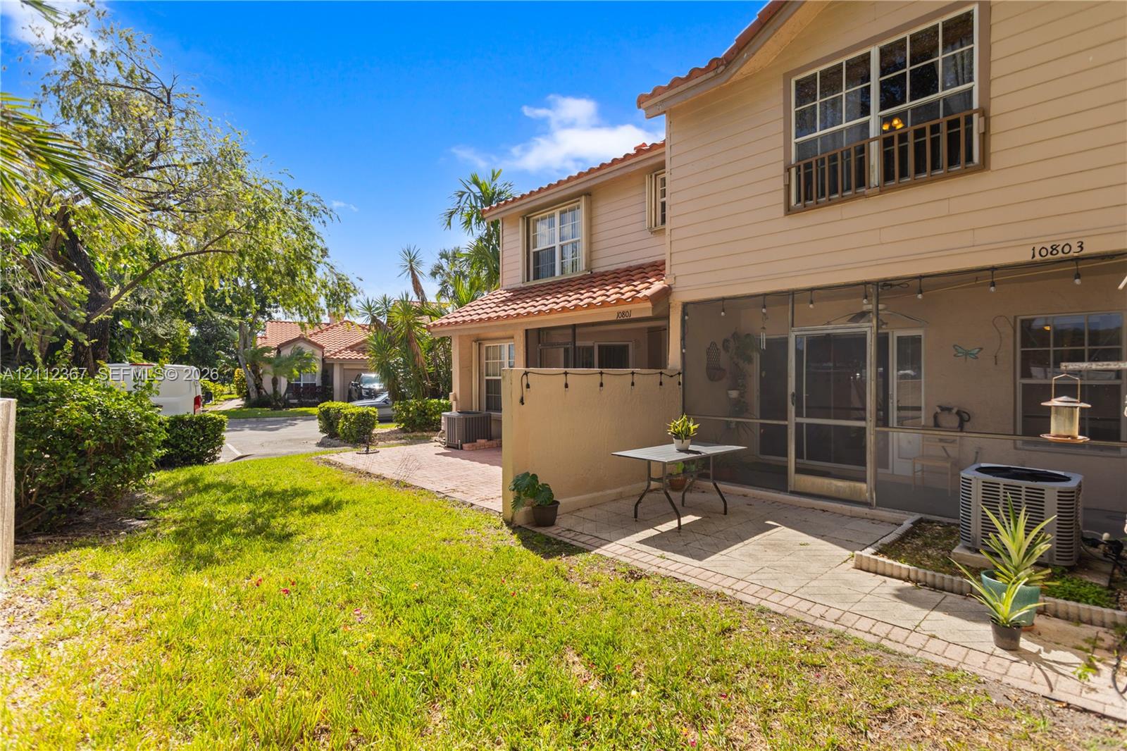 Exterior featuring two-story beige siding, tile roof, screened-in porch, paved patio, and grass lawn