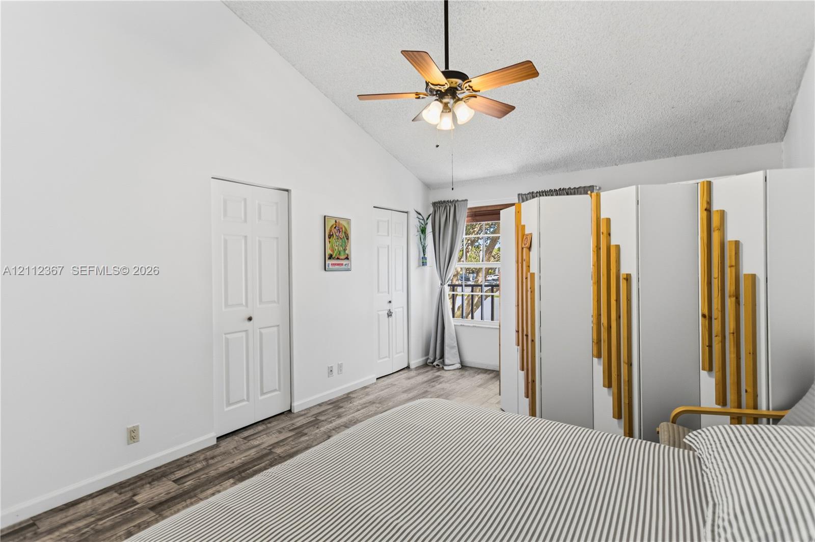 Vaulted ceiling with a centrally mounted ceiling fan, wood-finish flooring, and two interior doors featuring white-finished panels