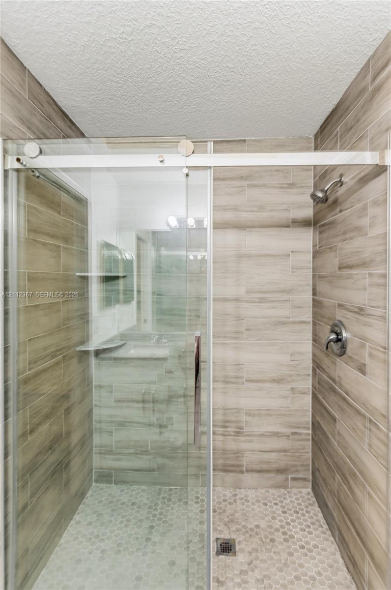 Walk-in shower featuring wood-finish tile surround, sliding glass door with stainless steel hardware, integrated corner shelving, and circular mosaic tile flooring
