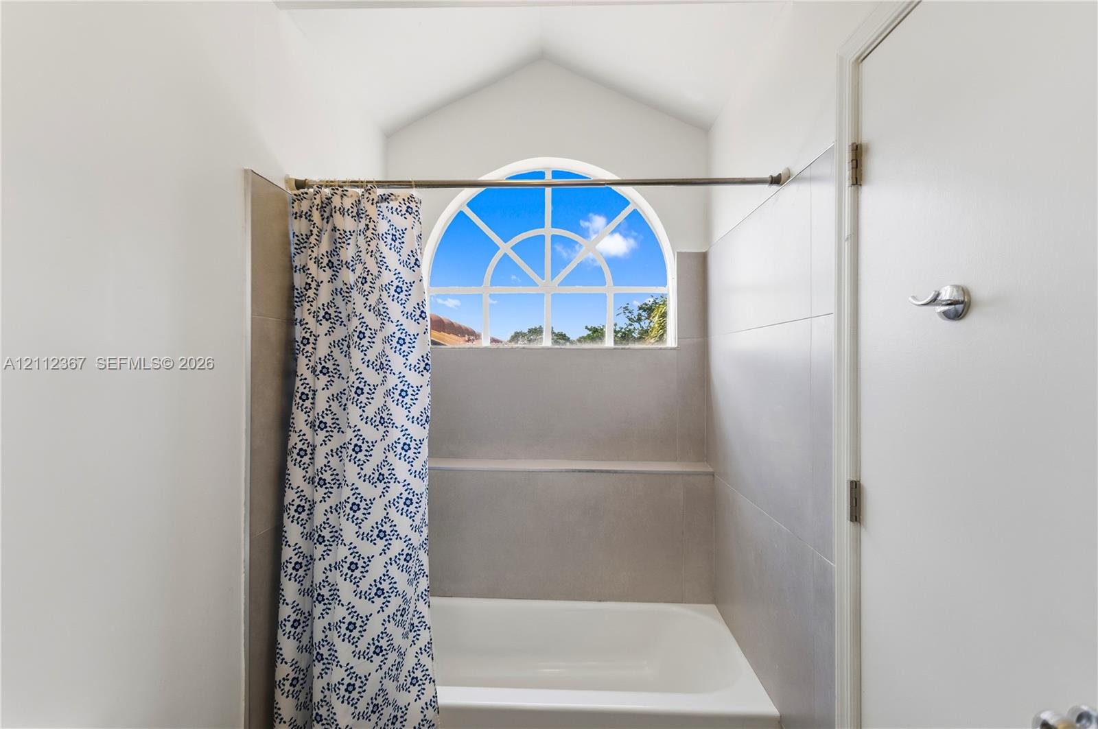 Vaulted ceiling, arched window with muntins, neutral wall tiles, and built-in recessed shelf