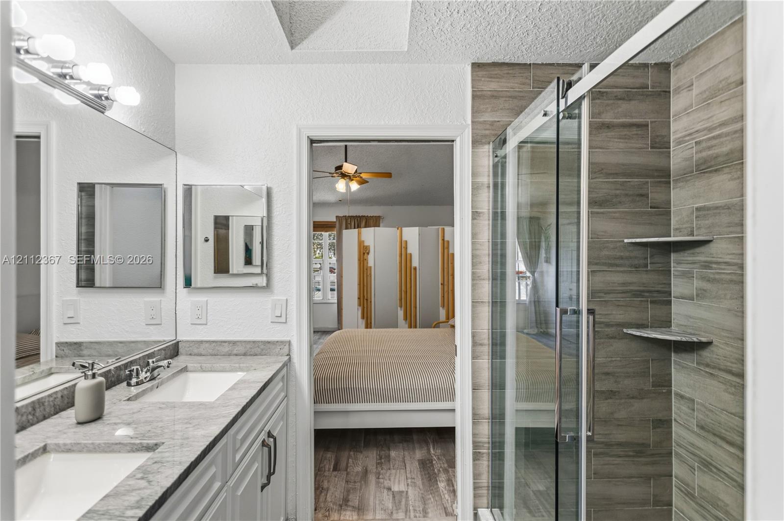 Dual-sink vanity with stone-finish countertop, full-width wall mirror, and walk-in shower with horizontal tile surround and integrated shelving