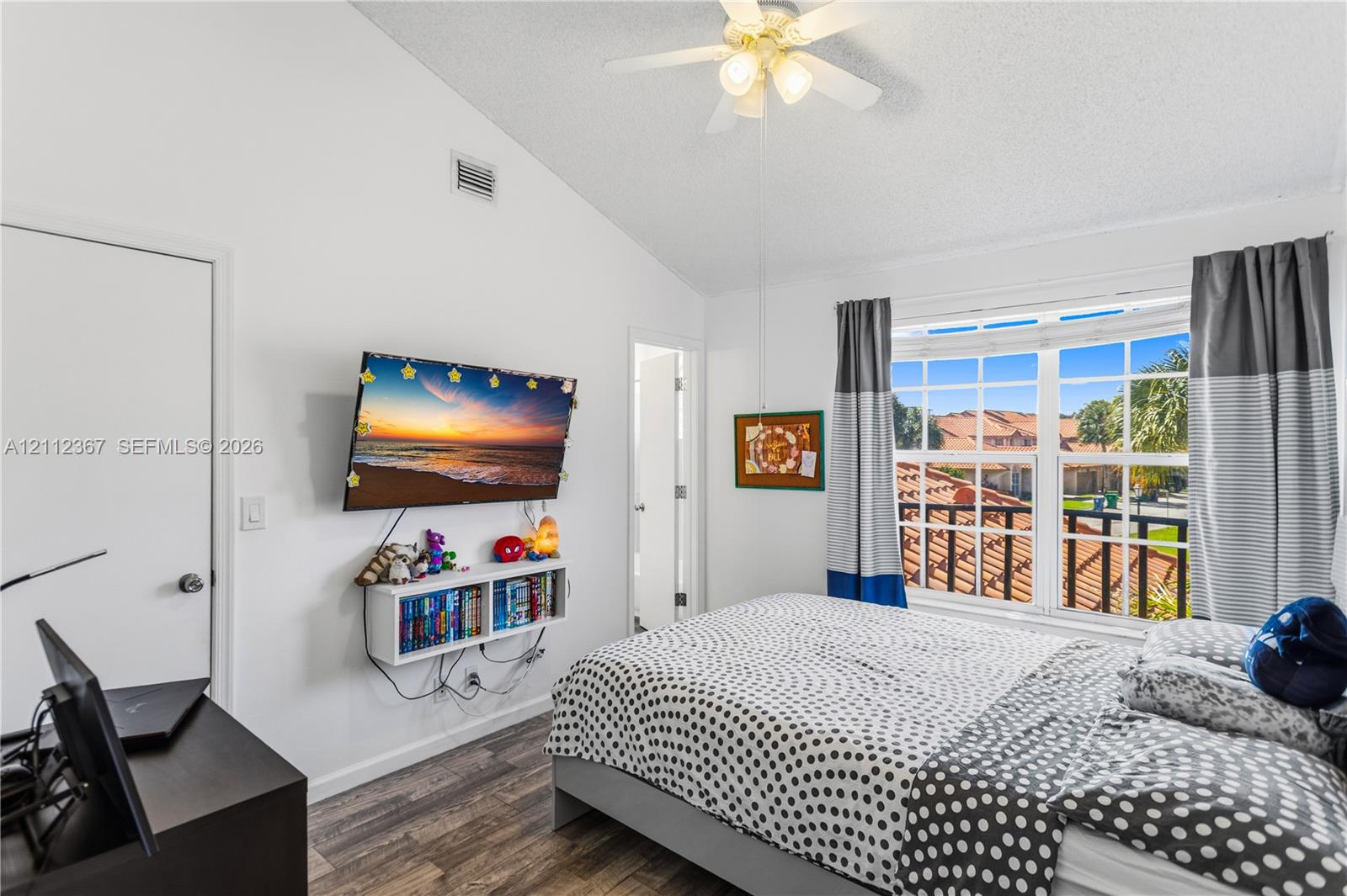 Vaulted ceiling with integrated multi-blade ceiling fan and wood-finish flooring, complemented by a large multi-pane window with grid detailing