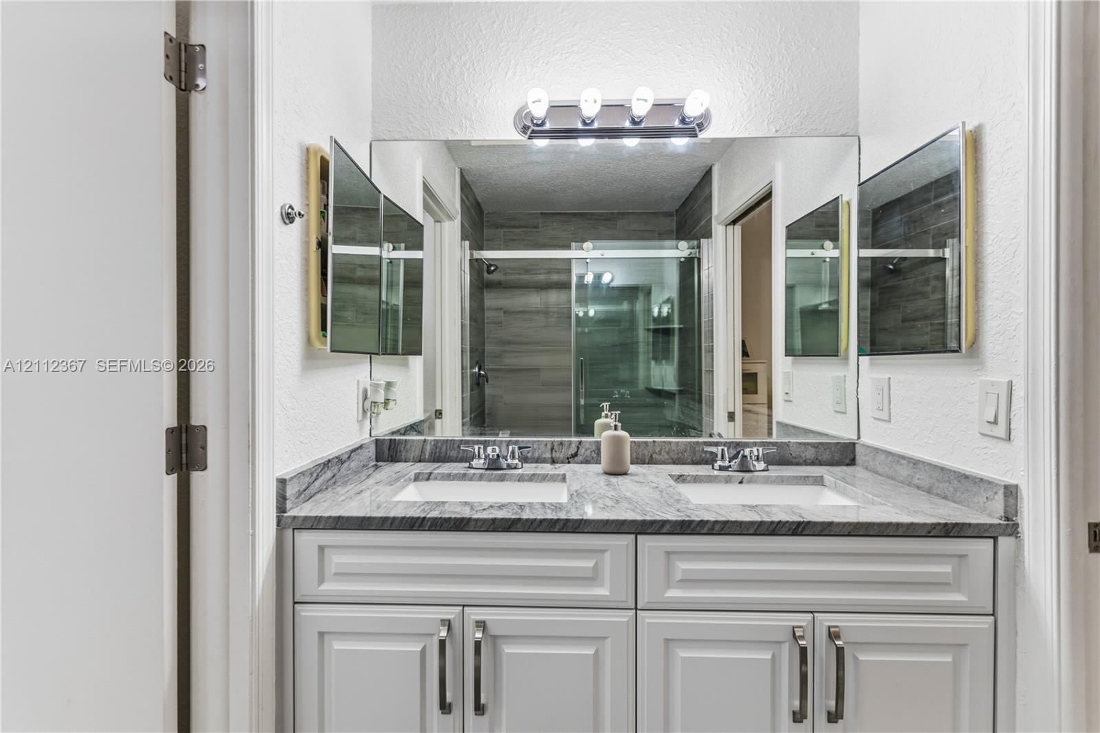 Double vanity featuring a stone countertop, dual undermount sinks, white cabinetry with silver hardware, and a large wall-mounted mirror