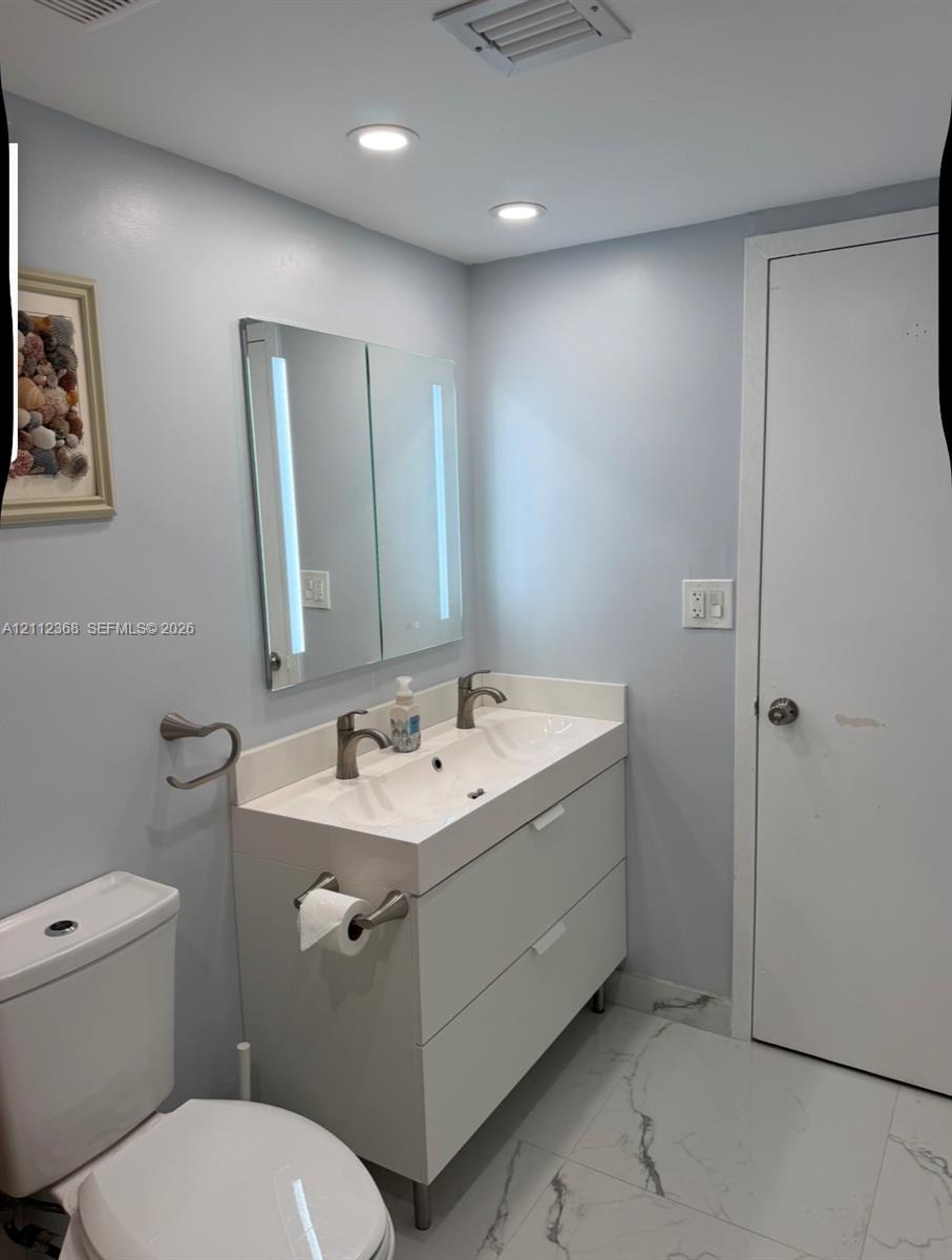 Modern dual-basin vanity featuring an integrated countertop, sleek matte-finish cabinetry, brushed-metallic fixtures, and a dual-panel lighted mirror, complemented by large-format stone-finish floor tiling