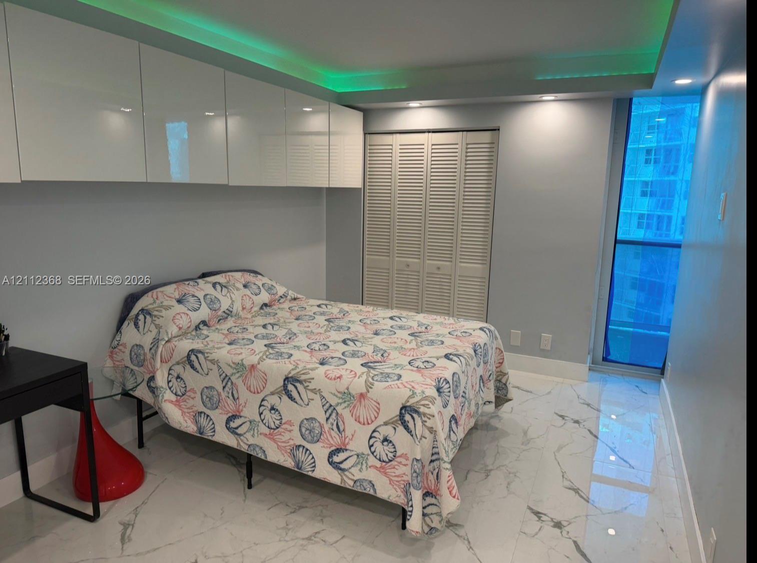 High-gloss white wall-mounted cabinetry, polished stone-look tile flooring, louvered closet doors, recessed ceiling lighting, and floor-to-ceiling glass paneling