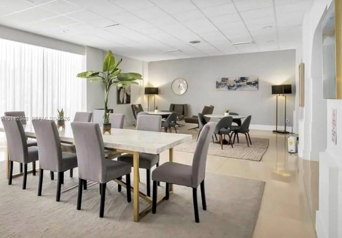 Open-concept room featuring a drop ceiling, expansive windows with floor-to-ceiling sheer drapery, and polished tile flooring