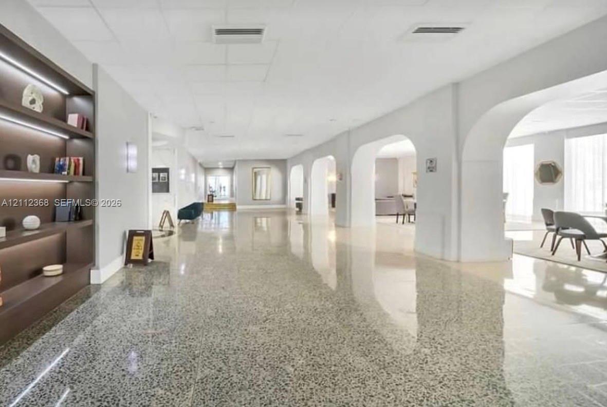 Spacious hallway featuring polished terrazzo flooring, integrated recessed shelving with ambient lighting, and decorative arched architectural openings