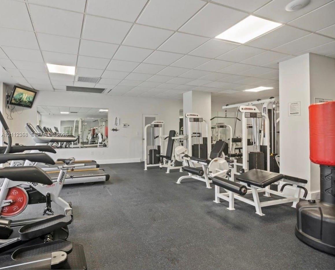Fitness area featuring drop ceiling panels, recessed lighting, wall-to-wall mirrors, and durable rubber flooring