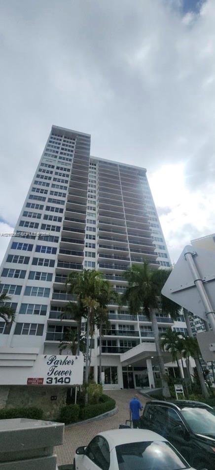 High-rise residential exterior featuring expansive private balconies, a covered porte-cochre entrance, and mature palm landscaping