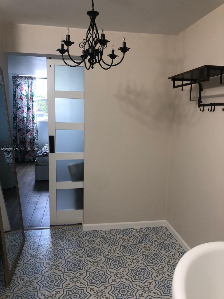 Patterned tile flooring, frosted glass sliding barn door with black hardware, ornate black metal chandelier, and wall-mounted metal shelf with integrated hooks