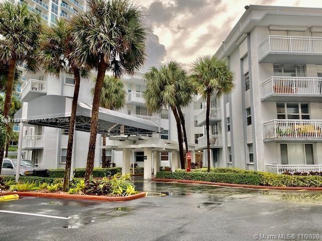 Multi-story residential complex featuring covered porte-cochre entry, balconies with railing systems, and landscaped grounds with mature palm trees Multi-story residential complex featuring covered porte-cochre entry, balconies with railing systems, and landscaped grounds with mature palm trees