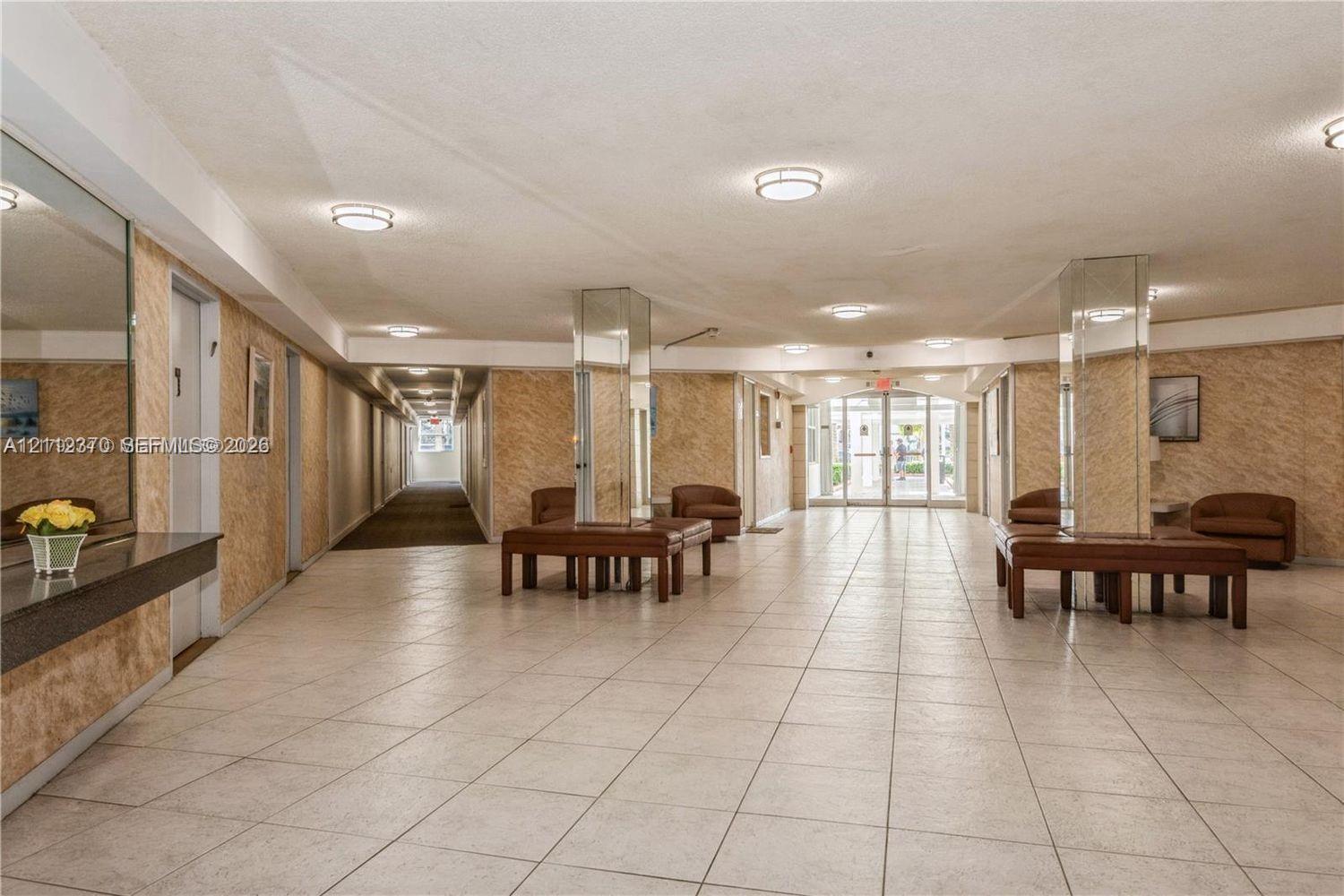 Common area featuring large-format tile flooring, mirrored structural pillars, textured wall surfaces, recessed ceiling lighting, and a glass-paneled entry door Common area featuring large-format tile flooring, mirrored structural pillars, textured wall surfaces, recessed ceiling lighting, and a glass-paneled entry door