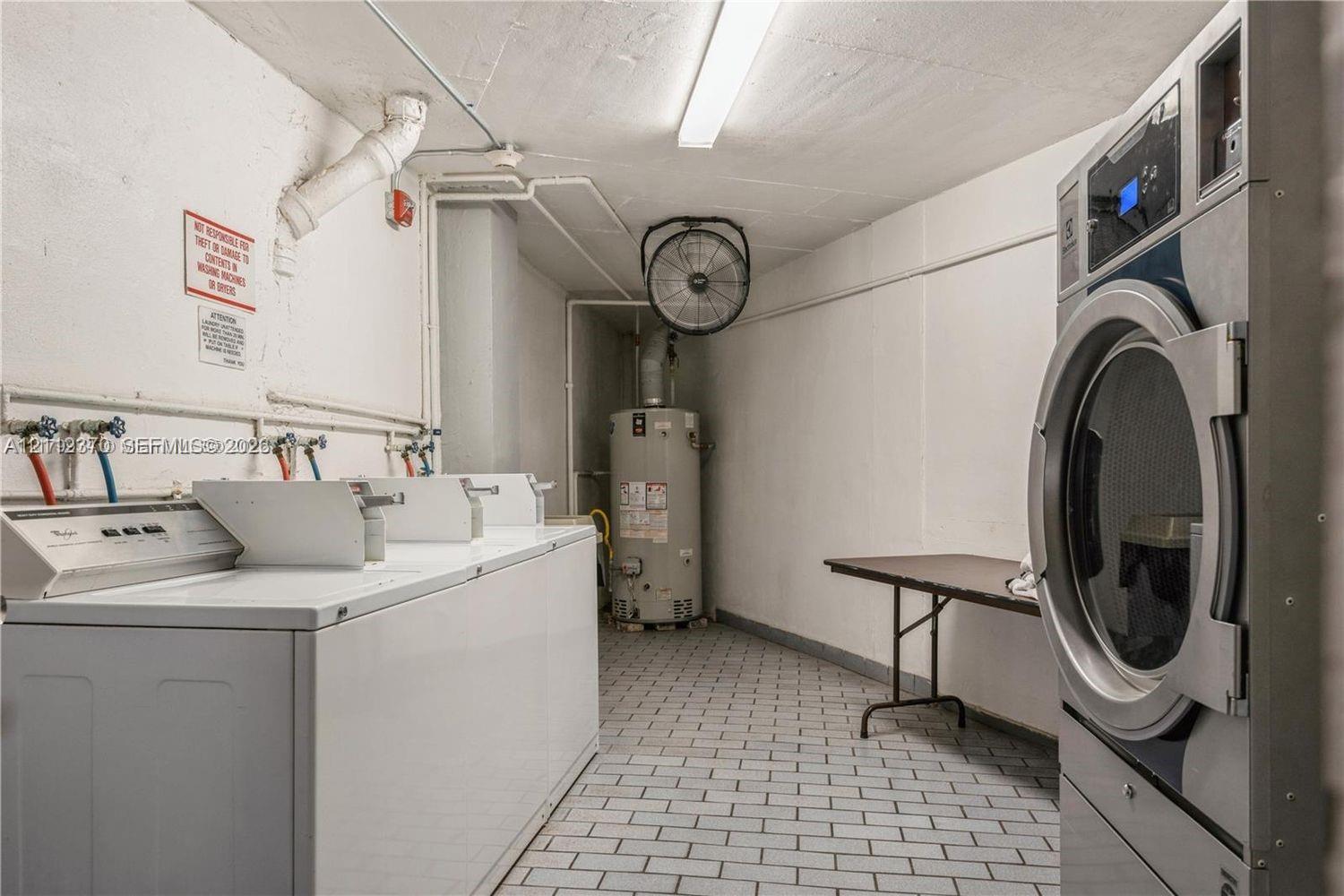 Laundry area featuring multiple washing machines, a large-capacity dryer, a dedicated water heater, and tiled flooring Laundry area featuring multiple washing machines, a large-capacity dryer, a dedicated water heater, and tiled flooring