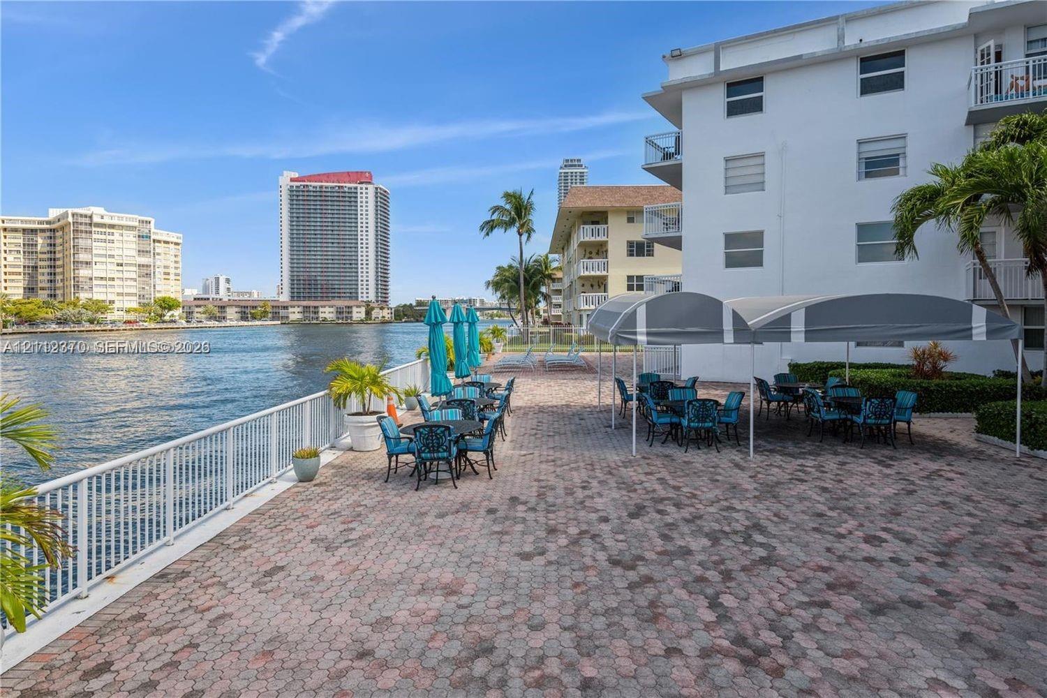 Waterfront terrace featuring stone paver flooring, white metal railing, and arched fabric awnings Waterfront terrace featuring stone paver flooring, white metal railing, and arched fabric awnings