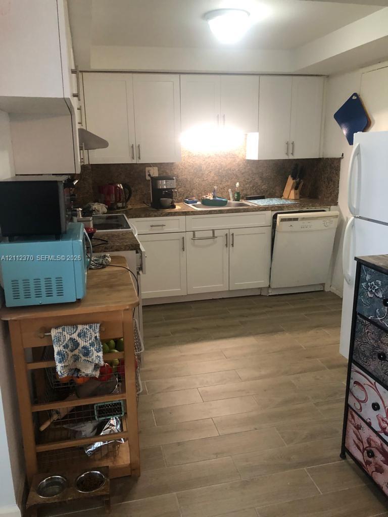 Kitchen featuring white cabinetry, stone-surface countertops, a stainless steel sink, integrated dishwasher, and wood-finish tile flooring
