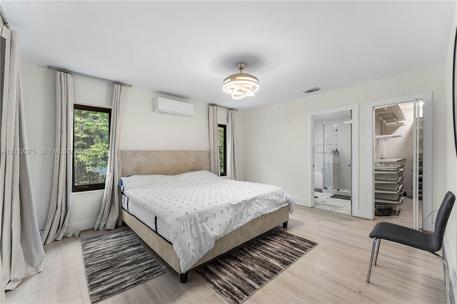 Light-filled room featuring wood-finish flooring, a wall-mounted ductless climate control unit, a modern multi-ring circular light fixture, and walk-in closet with custom shelving