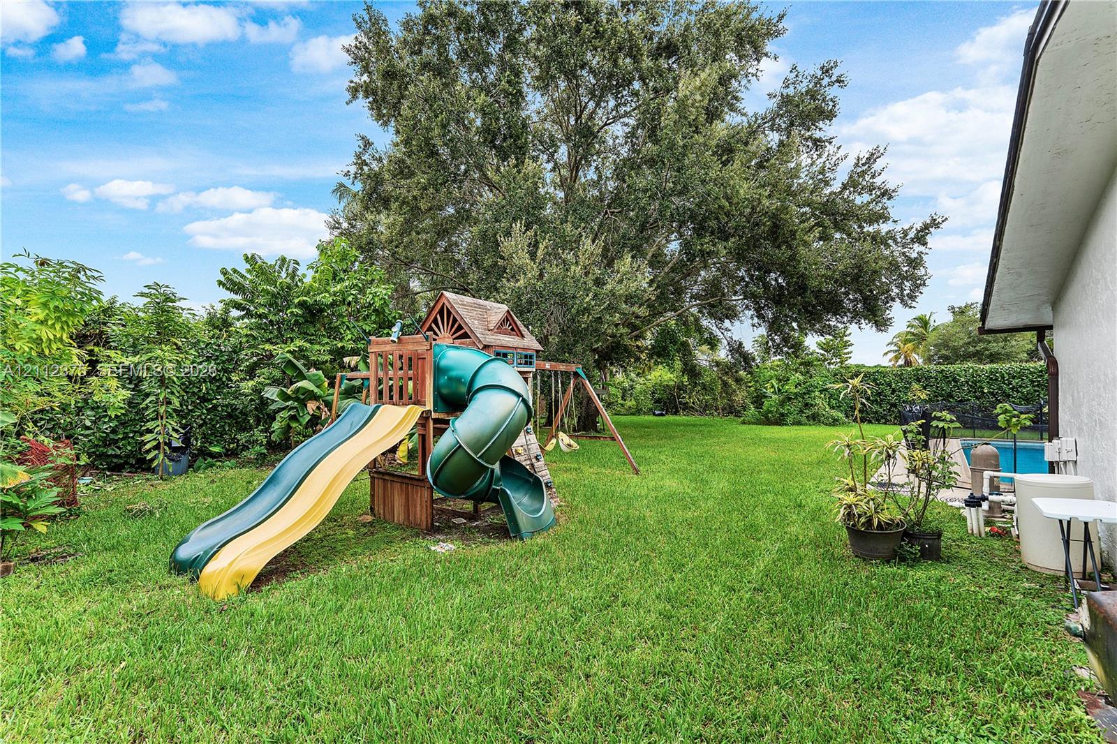 Expansive rear yard featuring a manicured lawn, mature trees, and perimeter hedging