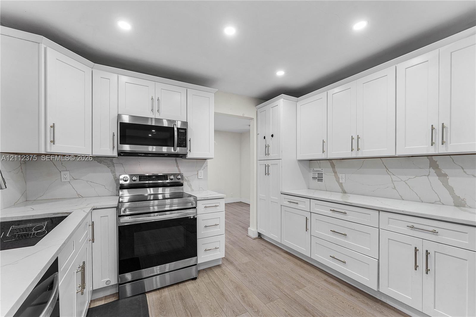 Kitchen featuring white Shaker-style cabinetry, stainless steel appliances, stone-patterned backsplash, quartz countertops, and wood-finish flooring