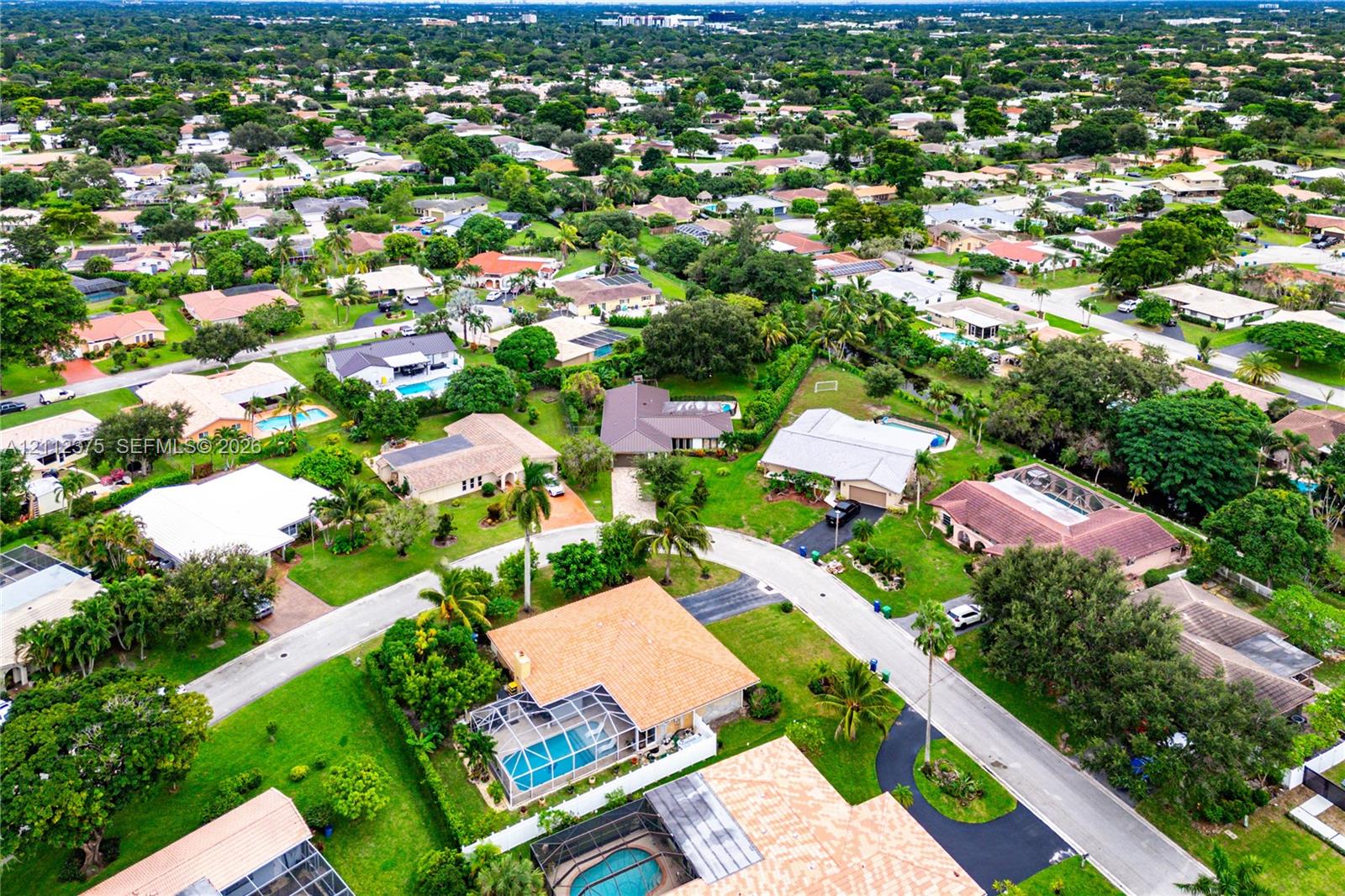 Aerial perspective of the residential property featuring a screened-in swimming pool, shingled roofing, paved driveway, and mature landscaping within a suburban setting