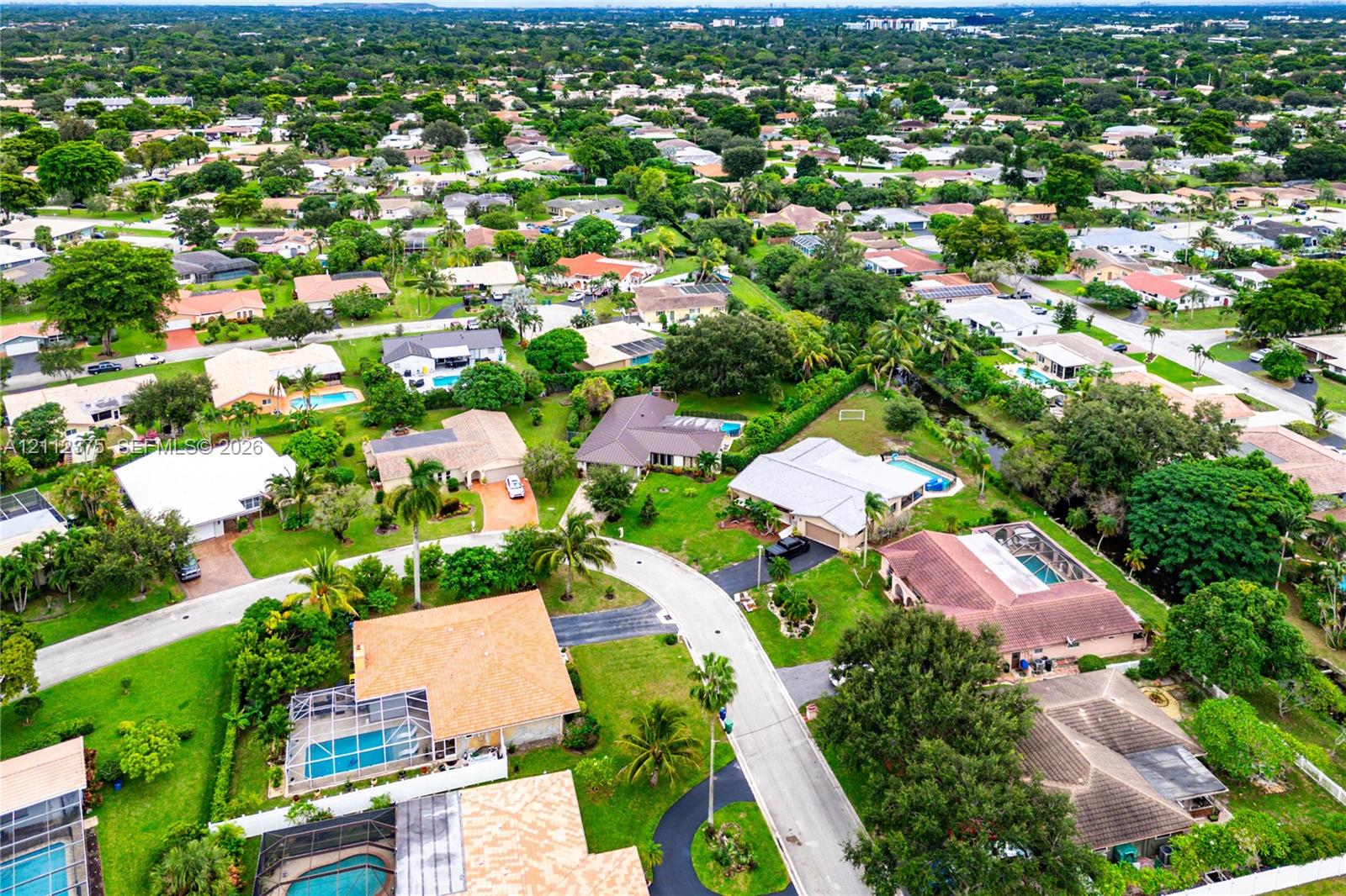 Aerial perspective of a suburban neighborhood featuring mature landscaping, paved roads, and residential properties with private swimming pools