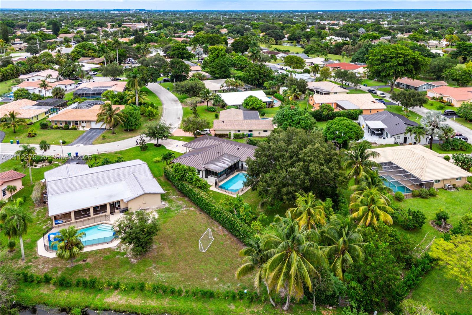 Aerial perspective of a suburban neighborhood featuring single-story residences with tiled roofs, screened-in swimming pools, expansive green lawns, and mature landscaping