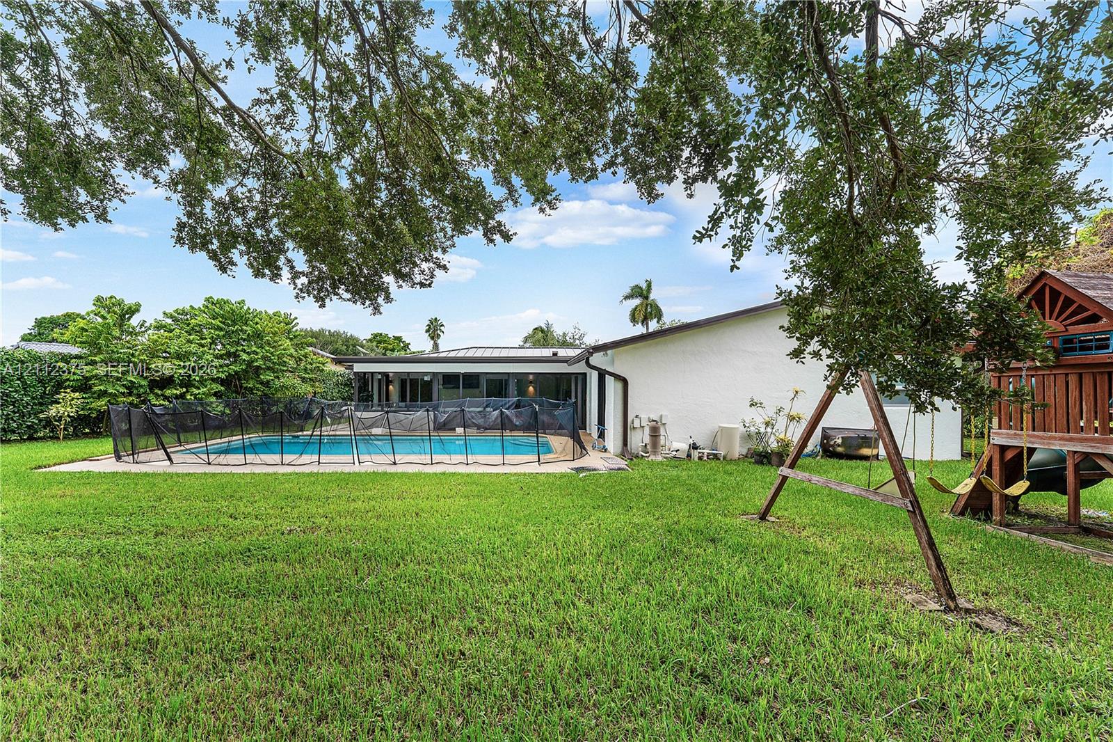Expansive backyard featuring a concrete-surround swimming pool and mature shade trees